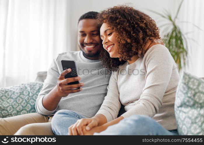 technology, internet and people concept - happy african american couple with smartphone at home. african american couple with smartphone at home