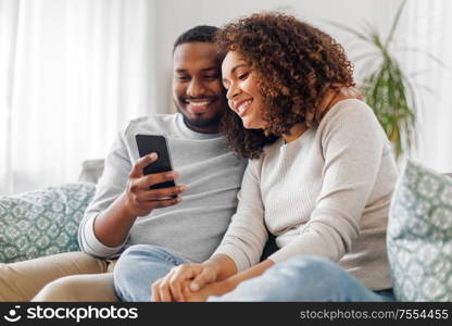 technology, internet and people concept - happy african american couple with smartphone at home. african american couple with smartphone at home