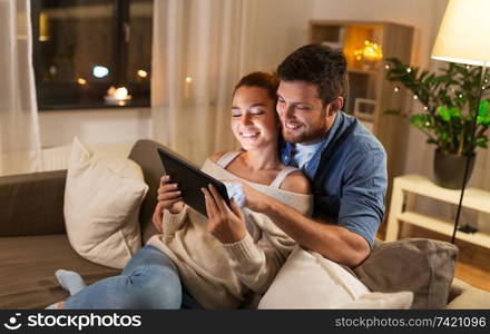 technology, internet and people concept - happy couple using tablet computer at home in evening. happy couple using tablet pc at home in evening