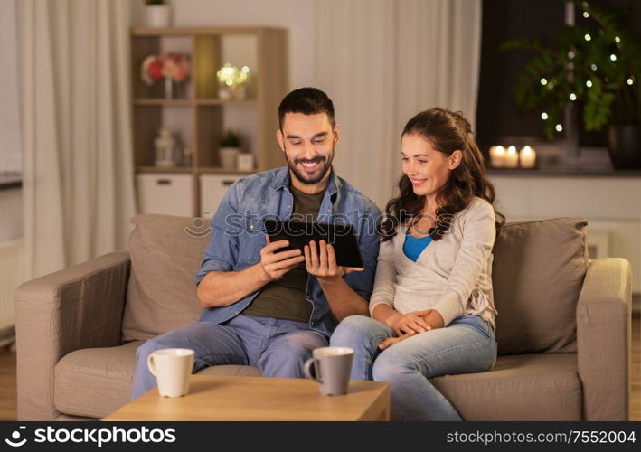 technology, internet and people concept - happy couple using tablet computer at home in evening. happy couple using tablet pc at home in evening