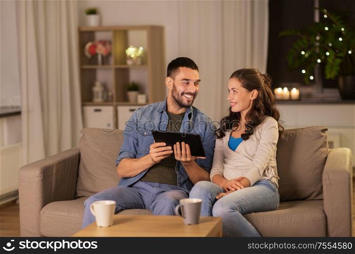 technology, internet and people concept - happy couple using tablet computer at home in evening. happy couple using tablet pc at home in evening