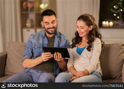 technology, internet and people concept - happy couple using tablet computer at home in evening. happy couple using tablet pc at home in evening