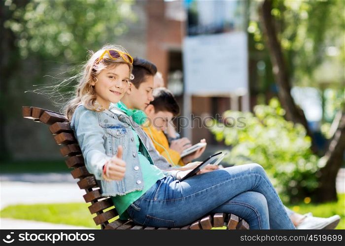 technology, internet and people concept - happy girl with tablet pc computer showing thumbs up and group of teenage friends or students outdoors