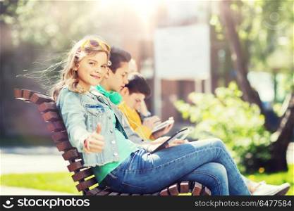 technology, internet and people concept - happy girl with tablet pc computer showing thumbs up and group of teenage friends or students outdoors. happy girl with tablet pc computer outdoors. happy girl with tablet pc computer outdoors