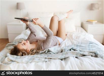 technology, internet and people concept - happy young woman lying in bed with tablet pc computer at home bedroom
