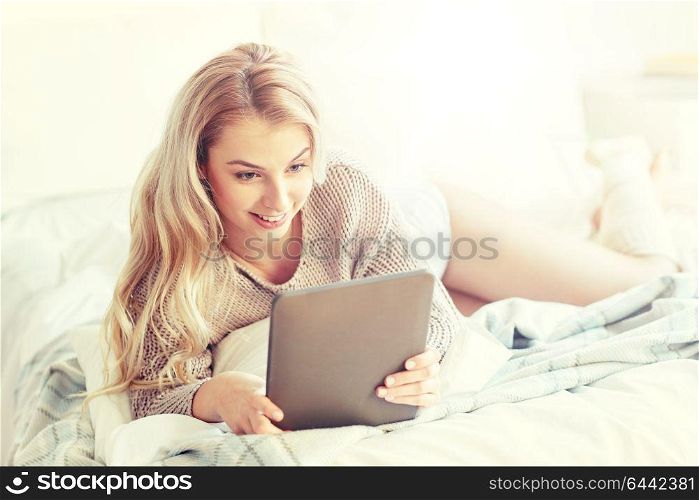 technology, internet and people concept - happy young woman lying in bed with tablet pc computer at home bedroom. happy young woman with tablet pc in bed at home