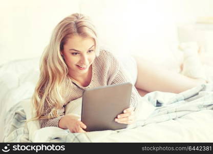 technology, internet and people concept - happy young woman lying in bed with tablet pc computer at home bedroom. happy young woman with tablet pc in bed at home