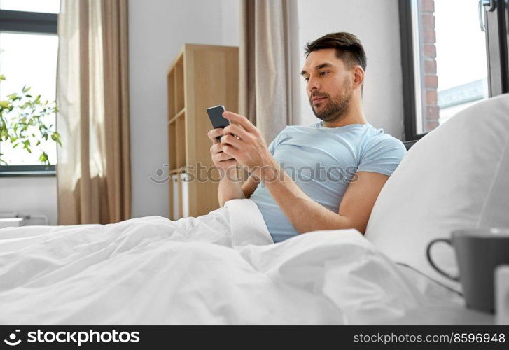 technology, internet and people concept - man texting on smartphone in bed at home in morning. man with smartphone in bed in morning at home