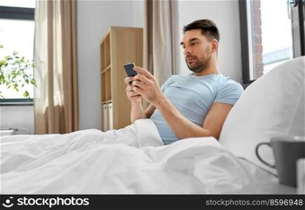 technology, internet and people concept - man texting on smartphone in bed at home in morning. man with smartphone in bed in morning at home