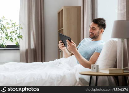 technology, internet and people concept - man with tablet pc computer in bed at home bedroom. man with tablet computer in bed at home bedroom