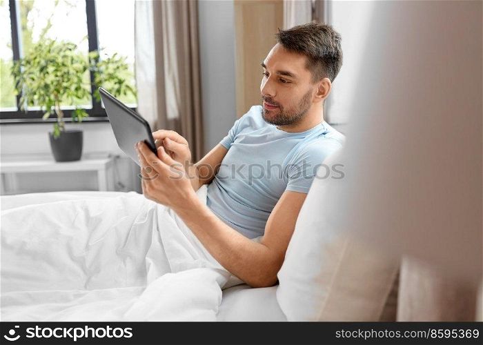 technology, internet and people concept - man with tablet pc computer in bed at home bedroom. man with tablet computer in bed at home bedroom