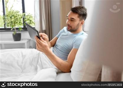 technology, internet and people concept - man with tablet pc computer in bed at home bedroom. man with tablet computer in bed at home bedroom