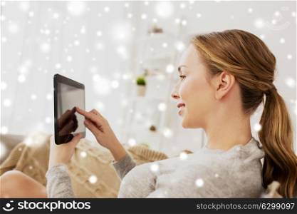 technology, internet and people concept - smiling woman sitting on couch with tablet pc computer at home over snow. smiling woman with tablet pc at home