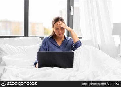 technology, internet and people concept - stressed young woman with laptop computer in bed at home bedroom. stressed young woman with laptop in bed at home