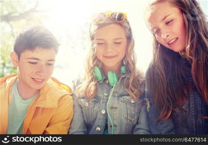 technology, internet and people concept - three happy teenage friends with headphones outdoors looking down at something. three happy teenage friends headphones. three happy teenage friends headphones