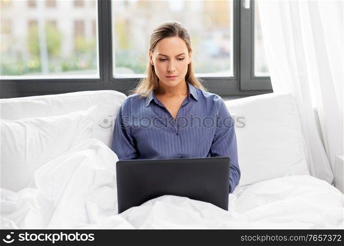 technology, internet and people concept - young woman with laptop computer in bed at home bedroom. young woman with laptop in bed at home bedroom