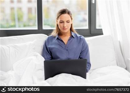 technology, internet and people concept - young woman with laptop computer in bed at home bedroom. young woman with laptop in bed at home bedroom