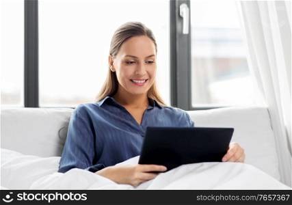technology, internet and people concept - young woman with tablet pc computer in bed at home bedroom. young woman with tablet pc in bed at home bedroom
