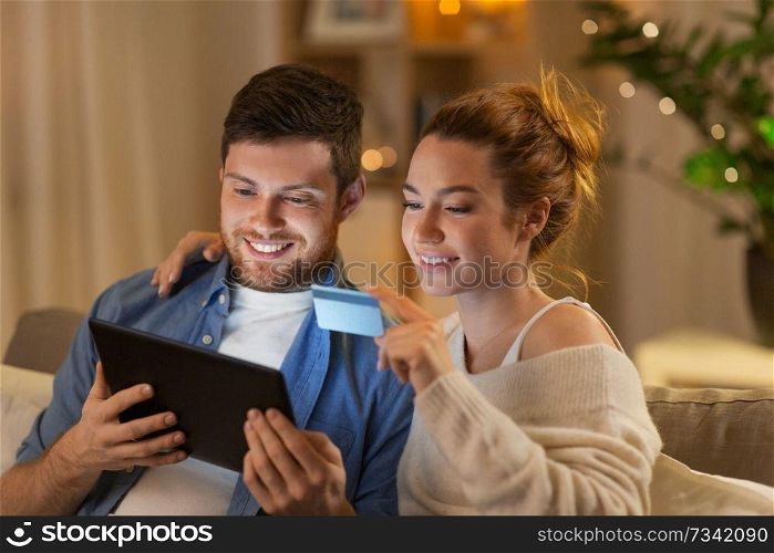 technology, internet banking and people concept - happy couple using tablet computer and credit card at home in evening. couple with tablet pc and credit card at home