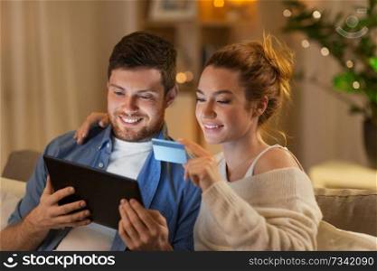 technology, internet banking and people concept - happy couple using tablet computer and credit card at home in evening. couple with tablet pc and credit card at home