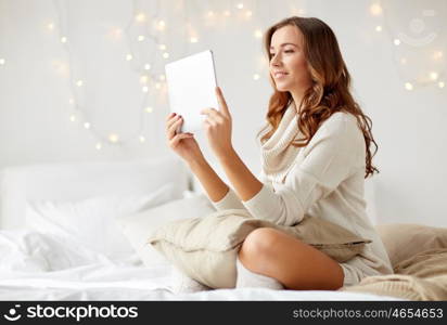 technology, internet, christmas and people concept - happy young woman lying in bed with tablet pc computer at home bedroom