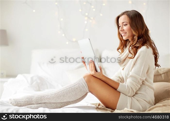 technology, internet, christmas and people concept - happy young woman lying in bed with tablet pc computer at home bedroom