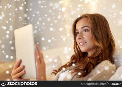 technology, internet, christmas and people concept - happy young woman lying in bed with tablet pc computer at home bedroom over snow. happy young woman with tablet pc in bed at home