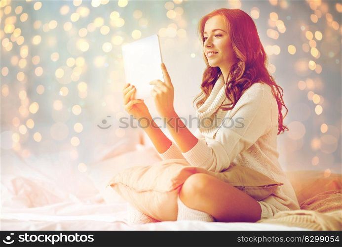 technology, internet, christmas and people concept - happy young woman lying in bed with tablet pc computer at home bedroom. happy young woman with tablet pc in bed at home