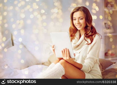 technology, internet, christmas and people concept - happy young woman lying in bed with tablet pc computer at home bedroom. happy young woman with tablet pc in bed at home