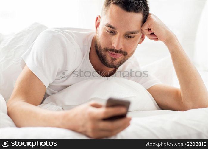 technology, internet, communication and people concept - close up of happy young man texting on smartphone in bed at home in morning. close up of man with smartphone in bed in morning