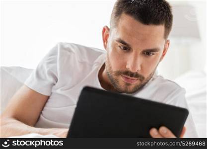 technology, internet, communication and people concept - close up of young man with tablet pc computer in bed at home. close up of man with tablet pc in bed at home