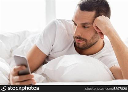 technology, internet, communication and people concept - close up of young man texting on smartphone in bed at home in morning. close up of man with smartphone in bed in morning
