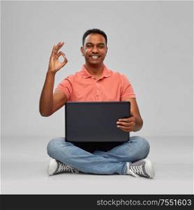 technology, internet, communication and people concept - happy indian man with laptop computer sitting on floor and showing ok hand sign over grey background. happy indian man with laptop computer showing ok
