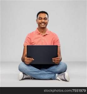 technology, internet, communication and people concept - happy indian man with laptop computer sitting on floor over grey background. happy indian man with laptop computer on floor