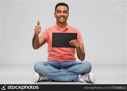 technology, internet, communication and people concept - happy indian man with tablet computer sitting on floor over grey background. happy indian man with tablet pc showing thumbs up