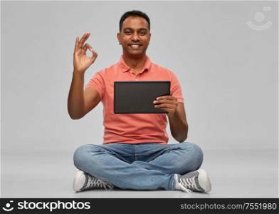 technology, internet, communication and people concept - happy indian man with tablet computer sitting on floor over grey background. happy indian man with tablet pc