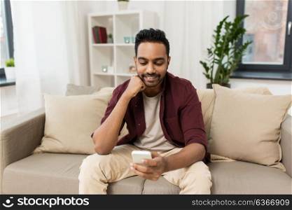 technology, internet, communication and people concept - happy smiling man texting on smartphone at home. happy man with smartphone at home