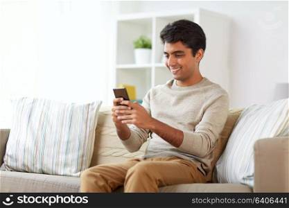 technology, internet, communication and people concept - happy smiling man texting on smartphone at home. happy man with smartphone at home