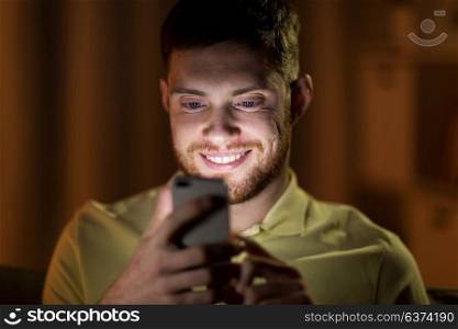 technology, internet, communication and people concept - happy smiling young man texting on smartphone in bed at home at night. happy young man with smartphone at night