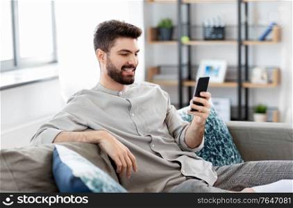 technology, internet, communication and people concept - happy smiling young man texting on smartphone at home. happy smiling young man with smartphone at home