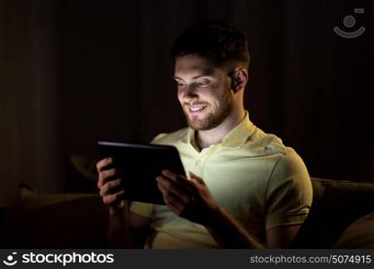 technology, internet, communication and people concept - happy smiling young man with tablet pc computer at night at home. young man with tablet pc computer at night