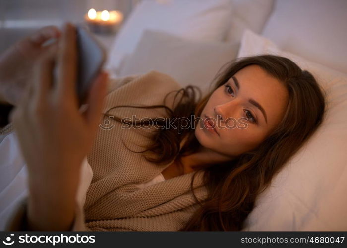 technology, internet, communication and people concept - happy smiling young woman texting on smartphone in bed at home bedroom at night