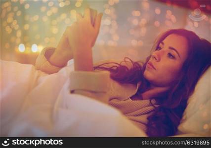 technology, internet, communication and people concept - happy smiling young woman texting on smartphone in bed at home bedroom at night. young woman with smartphone in bed at home bedroom