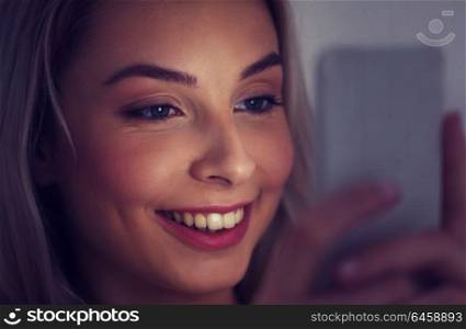 technology, internet, communication and people concept - happy smiling young woman texting on smartphone at home at night. happy smiling young woman with smartphone at night