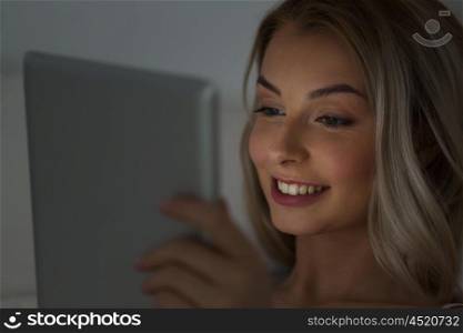 technology, internet, communication and people concept - happy smiling young woman with tablet pc computer in bed at home bedroom at night