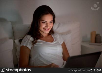 technology, internet, communication and people concept - happy smiling young woman with laptop computer in bed at home bedroom at night. happy woman with laptop in bed at home bedroom