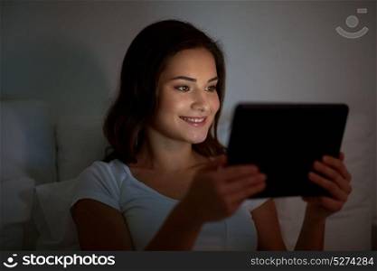 technology, internet, communication and people concept - happy smiling young woman with tablet pc computer in bed at home bedroom at night. young woman with tablet pc in bed at home bedroom