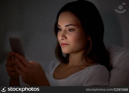 technology, internet, communication and people concept - happy young woman with smartphone in bed at home at night. happy young woman with smartphone in bed at night