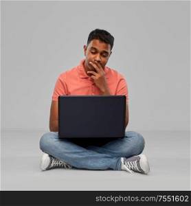 technology, internet, communication and people concept - thinking indian man with laptop computer sitting on floor over grey background. thinking indian man with laptop computer