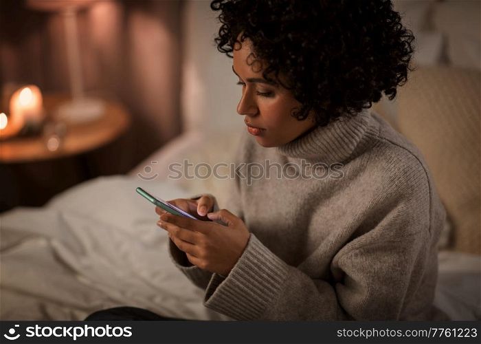 technology, internet, communication and people concept - woman with smartphone sitting in bed at home at night. woman with smartphone sitting in bed at night